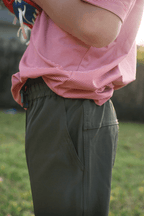 Boy wearing forest green pants and a red and white striped polo standing in a grassy field