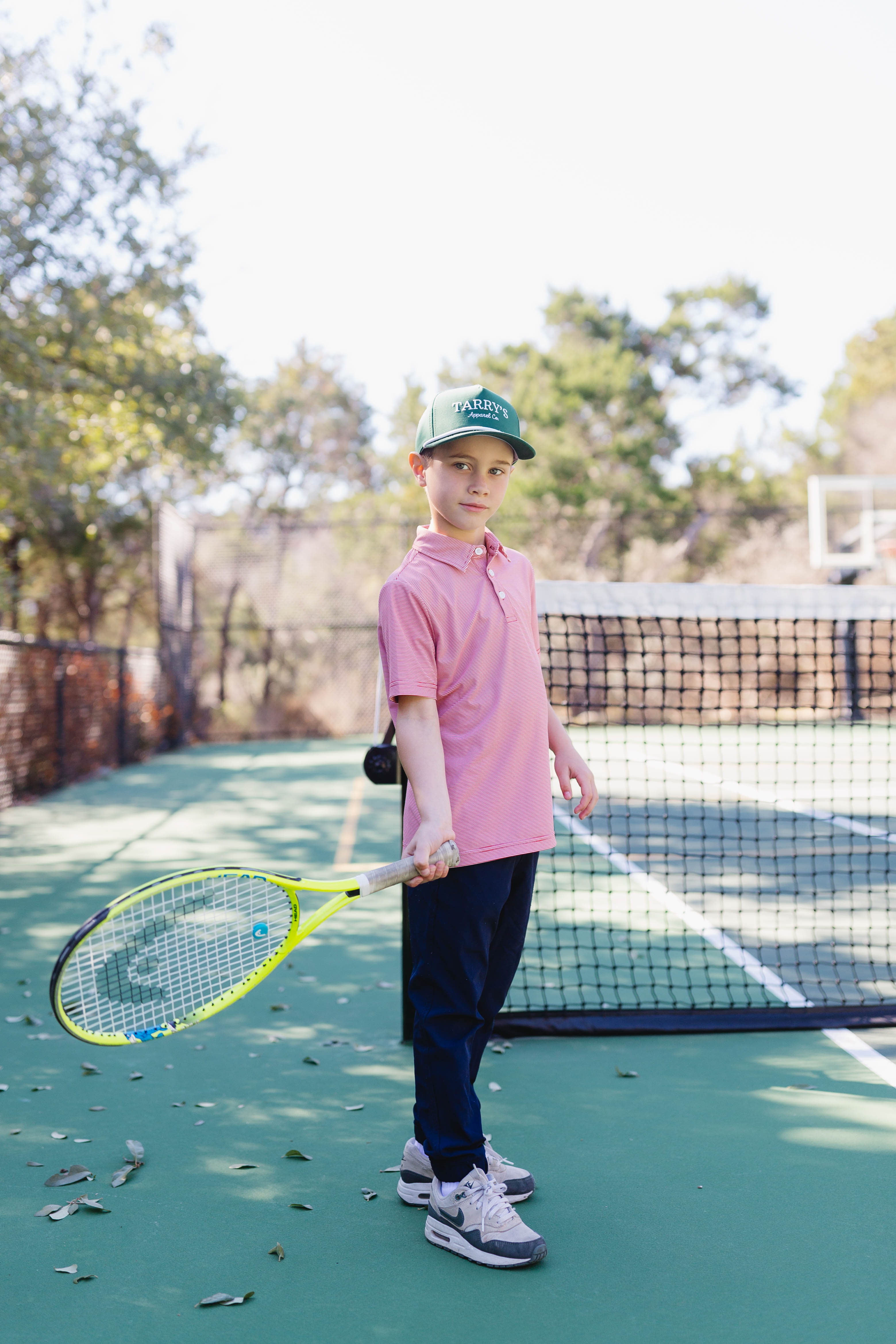 Boy wearing navy pants and a red and white polo playing on a tennis court holding a tennis racket