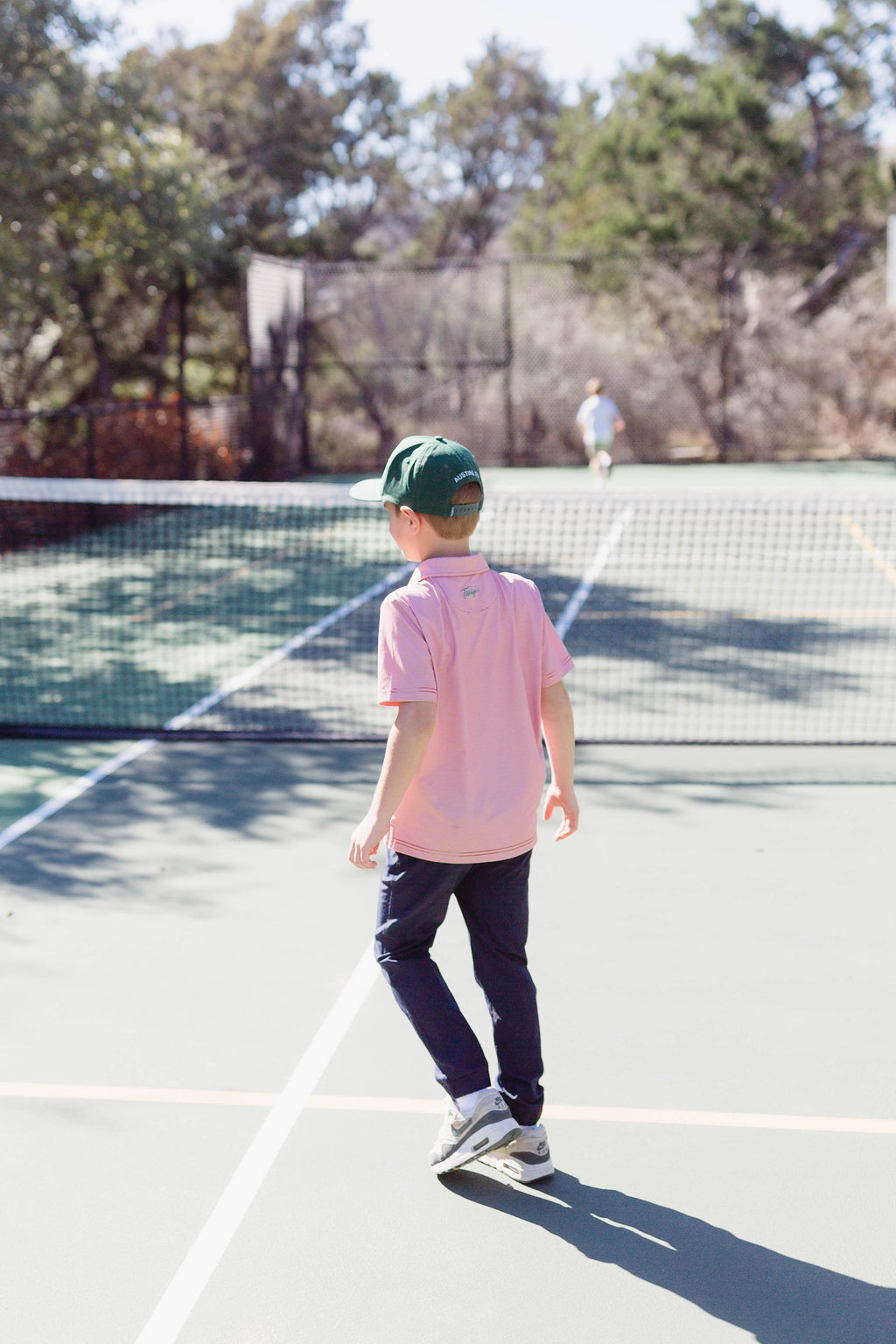 Boy wearing navy pants and a red and white polo playing on a tennis court