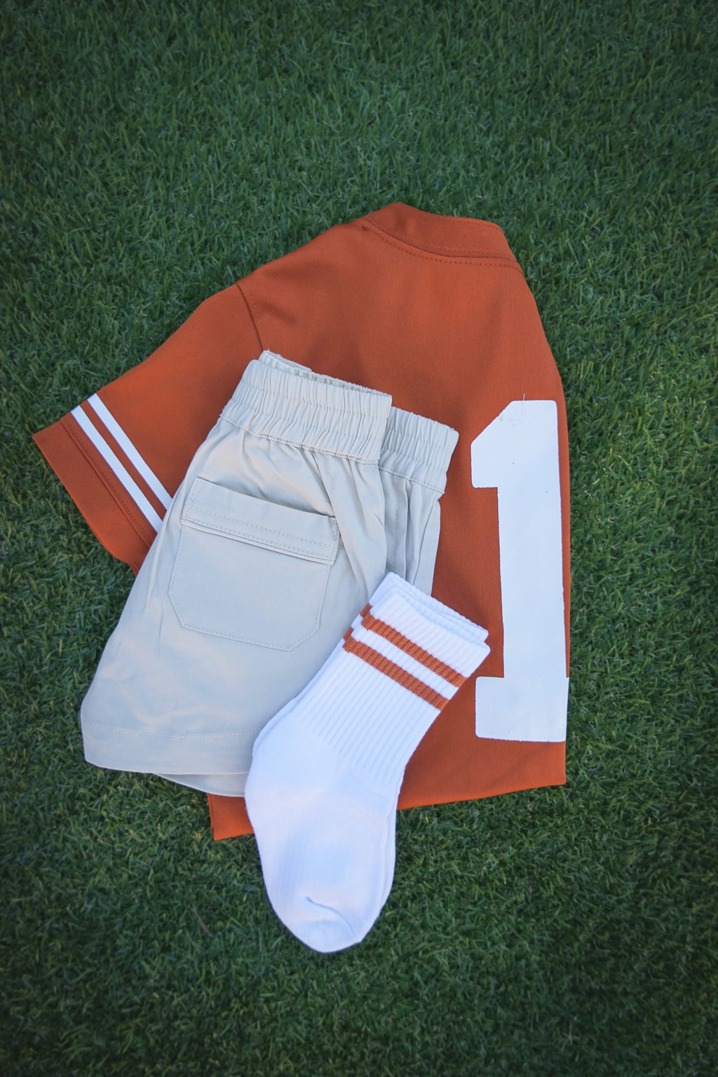 Texas orange sports jersey, boys khaki shorts, and white socks with burnt orange stripes on a green grass background