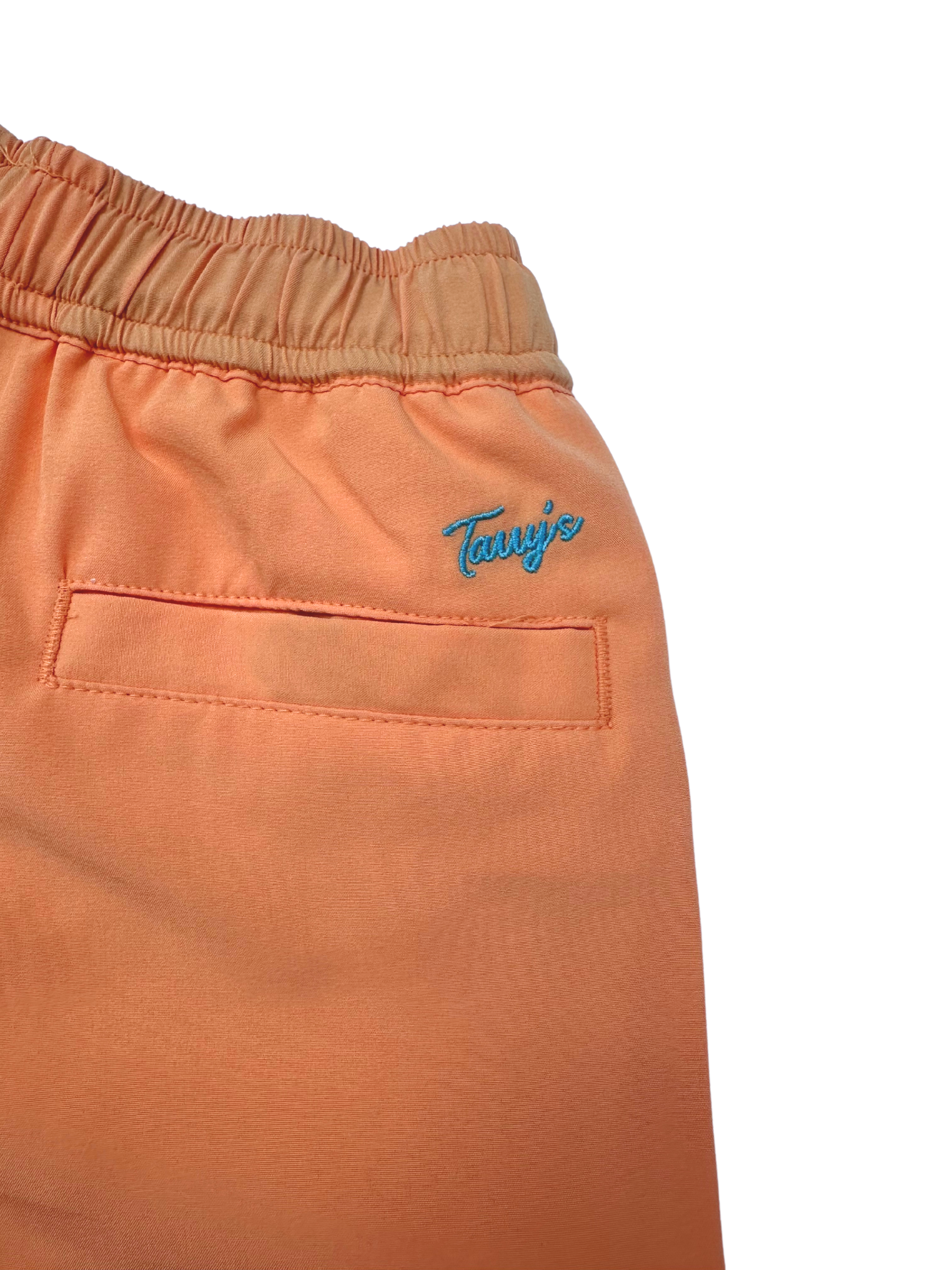 Close up of orange boys swim shorts with a blue logo on a white background